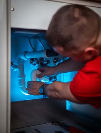 Plumber working on the drain trap beneath a sink